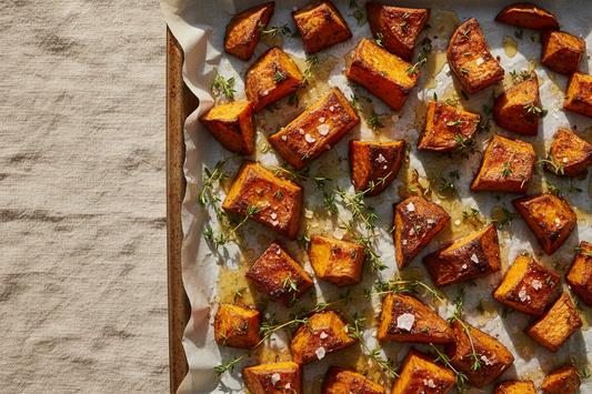 Brown butter honey roasted sweet potato chunks on a baking sheet with fresh thyme sprigs and flaky sea salt