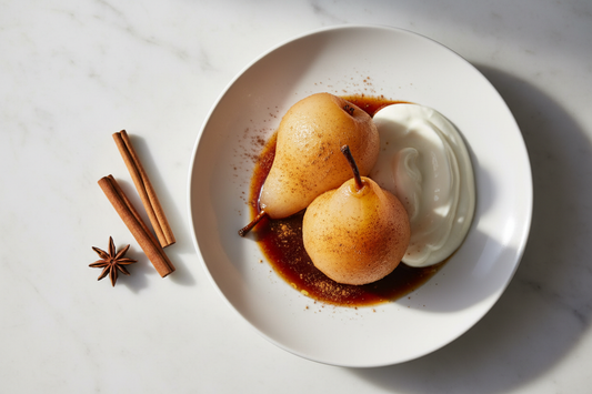 Two whole Ceylon cinnamon poached pears on a ceramic plate, translucent and golden-amber, drizzled with reduced spiced syrup and a dusting of cinnamon — a metabolic-friendly dessert from The Spice Apothecary.