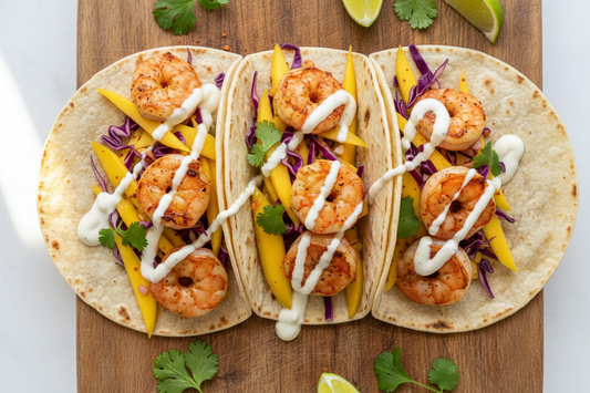 Chilli-lime shrimp tacos with mango slaw and lime crema in warm corn tortillas on a wooden board, garnished with fresh cilantro