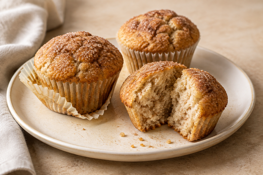 Homemade cinnamon sugar muffins with lightly golden tops on a cream plate, one split open to show the soft crumb