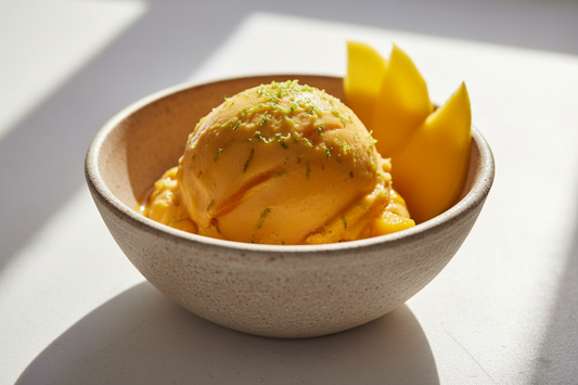 a golden-orange scoop of mango sorbet in a rustic bowl, garnished with lime zest and a mango slice