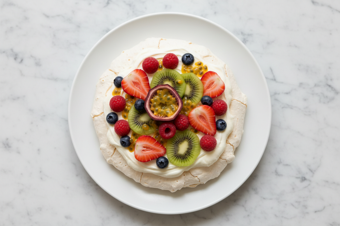 overhead shot of a fully topped pavlova on a white ceramic plate, whipped cream and fresh mixed fruit, white marble surface