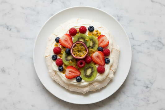 overhead shot of a fully topped pavlova on a white ceramic plate, whipped cream and fresh mixed fruit, white marble surface
