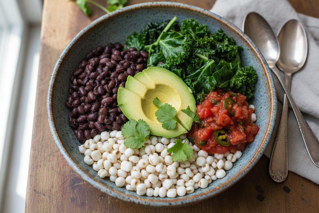Three Sisters grain bowl with hominy base topped with black beans, steamed kale and collard greens, sliced avocado, salsa, and