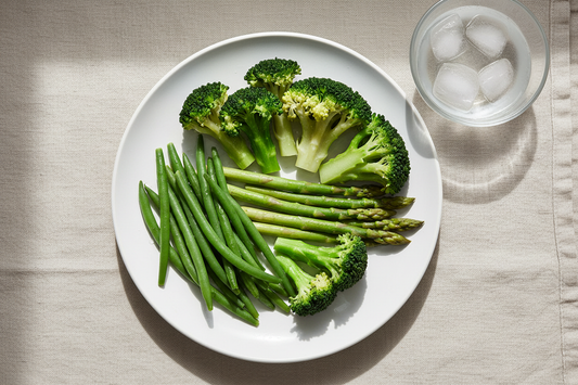 Perfectly blanched green vegetables including broccoli, green beans, and asparagus showing vibrant emerald colour on a white plate