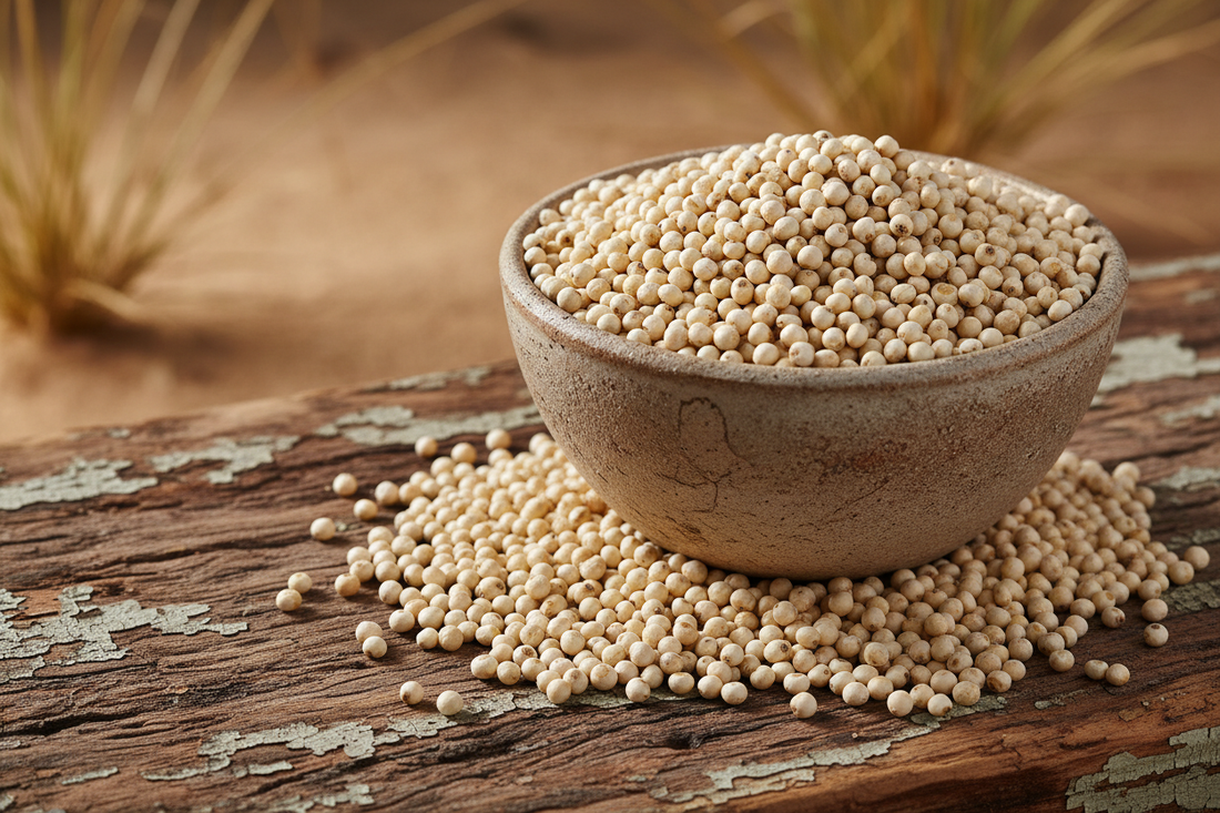 Whole white sorghum grains in rustic ceramic bowl on weathered wood showing pearl-like round grains